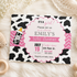 A customizable baby shower invitation card with a black and white cow print background, pink scalloped border, and pink chevron accents. The card features a baby bottle illustration and text reading 'IT'S A girl! Please join us as we celebrate EMILY'S baby shower'.