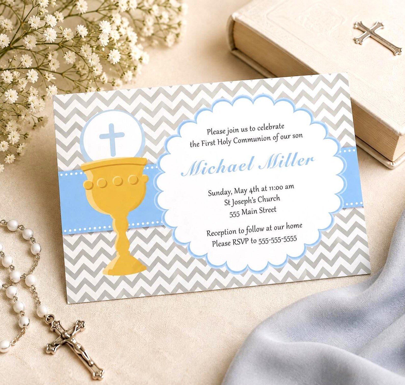 A First Holy Communion invitation card styled on a beige fabric background with a gold chalice, blue ribbon, gray and white chevron pattern, and religious props including a rosary, cross, and book.